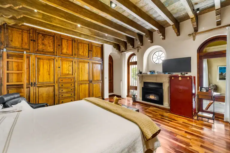 Casa 28 de Abril Norte, bedroom with built-in wood cabinets, a fireplace and a television under beamed ceilings, San Miguel de Allende