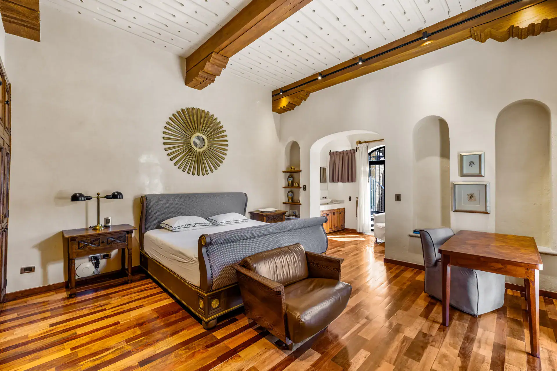 Casa 28 de Abril Norte, bedroom with a gray leather bed, sunburst mirror and a wood desk, San Miguel de Allende