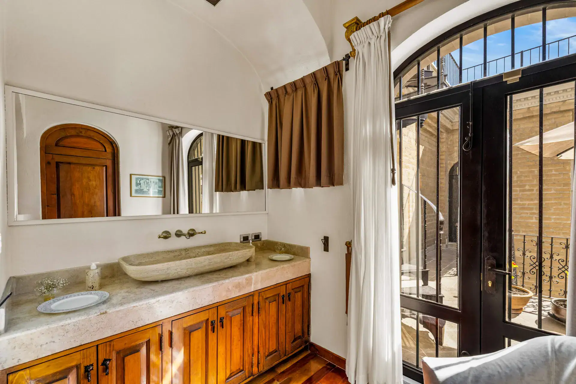 Casa 28 de Abril Norte, bathroom vanity with a stone trough sink and wood cabinets beside a barred balcony door, San Miguel de Allende