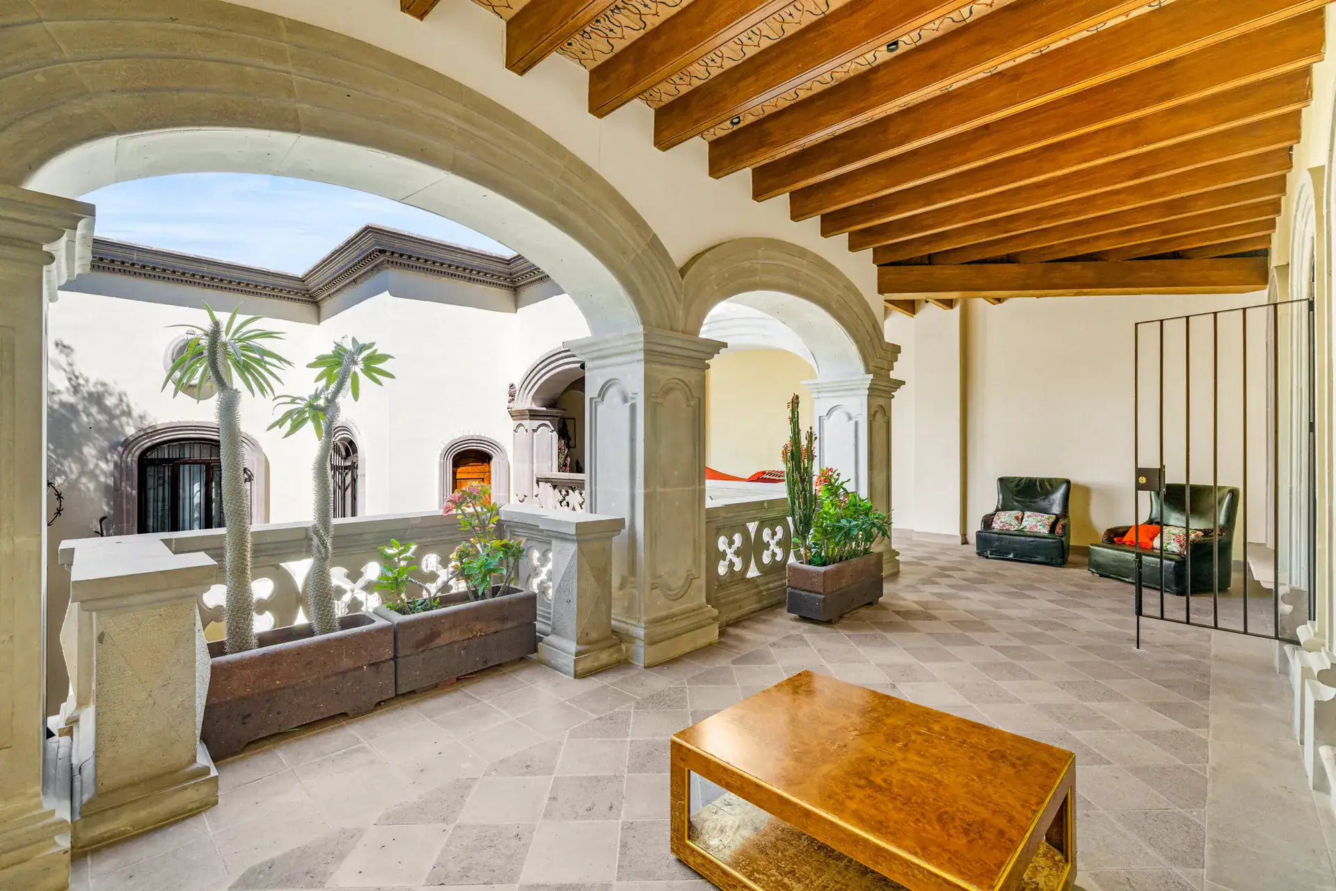 Casa 28 de Abril Norte, covered arcade overlooking the courtyard with a coffee table and green armchairs, San Miguel de Allende