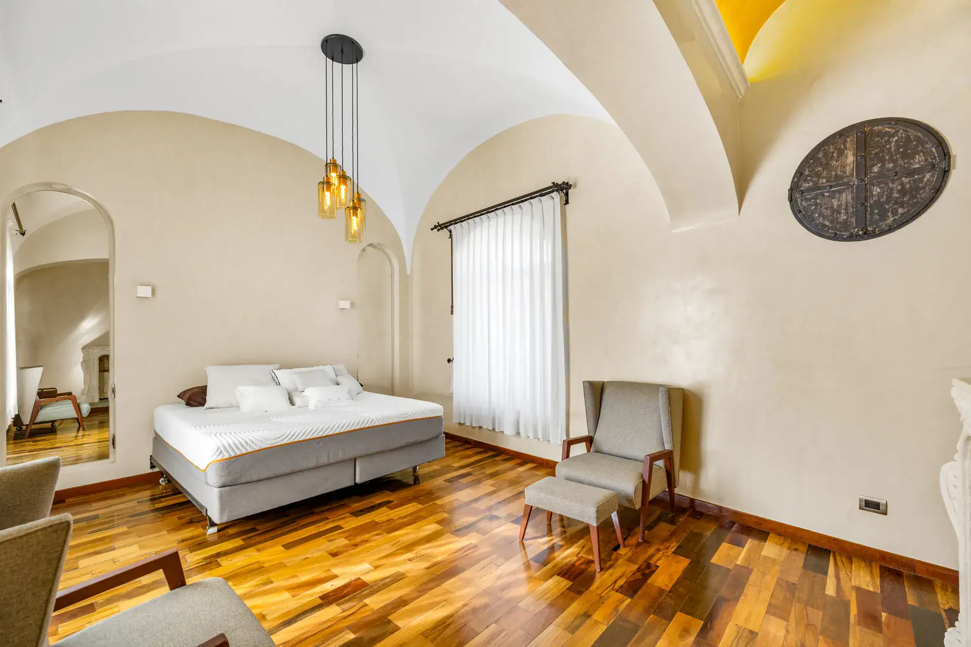 Casa 28 de Abril Norte, bedroom with a white bed, pendant lights, vaulted ceiling and a round wall ornament, San Miguel de Allende