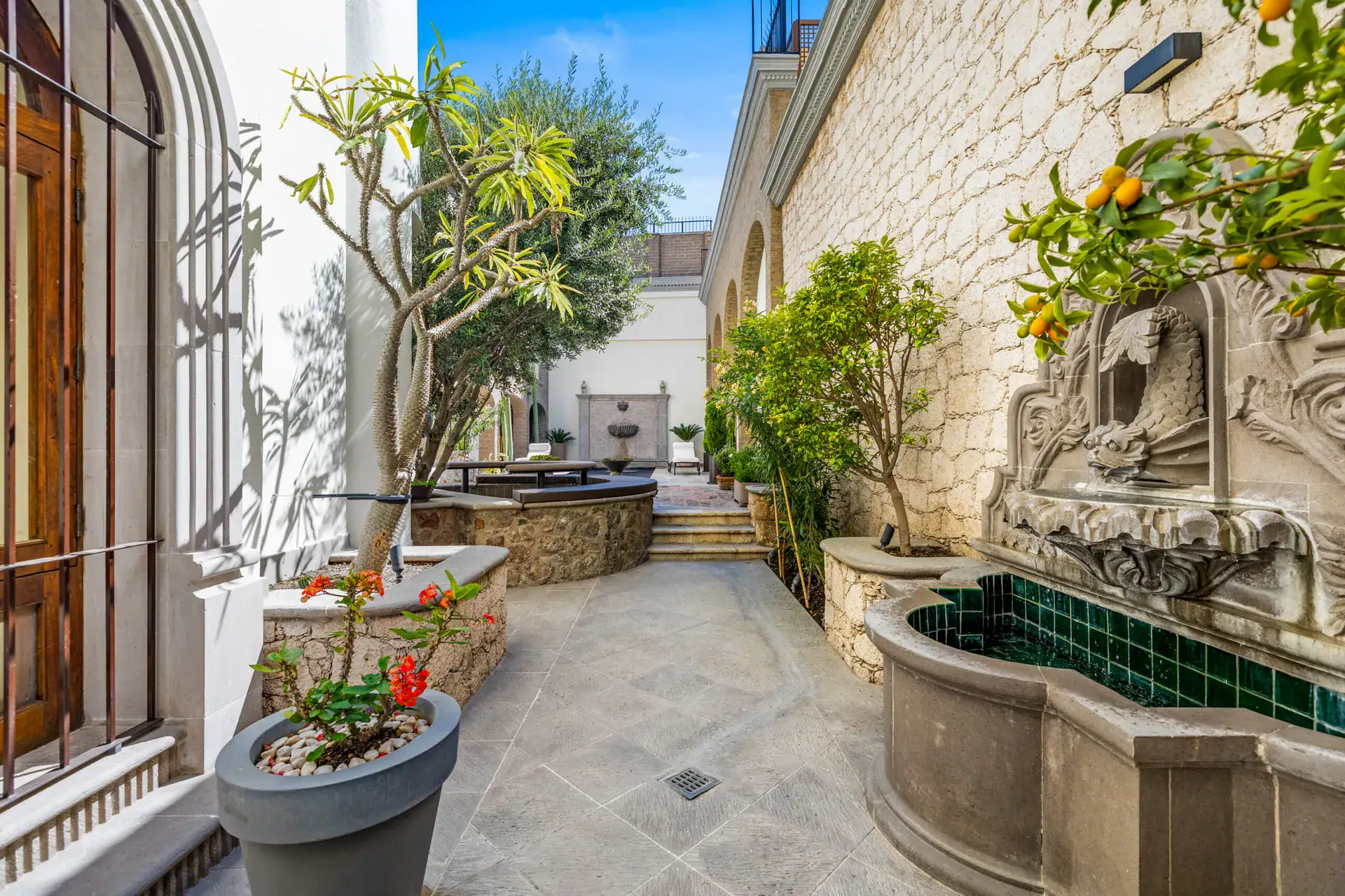 Casa 28 de Abril Norte, courtyard fountain beside a planter with citrus trees and a stone wall, San Miguel de Allende