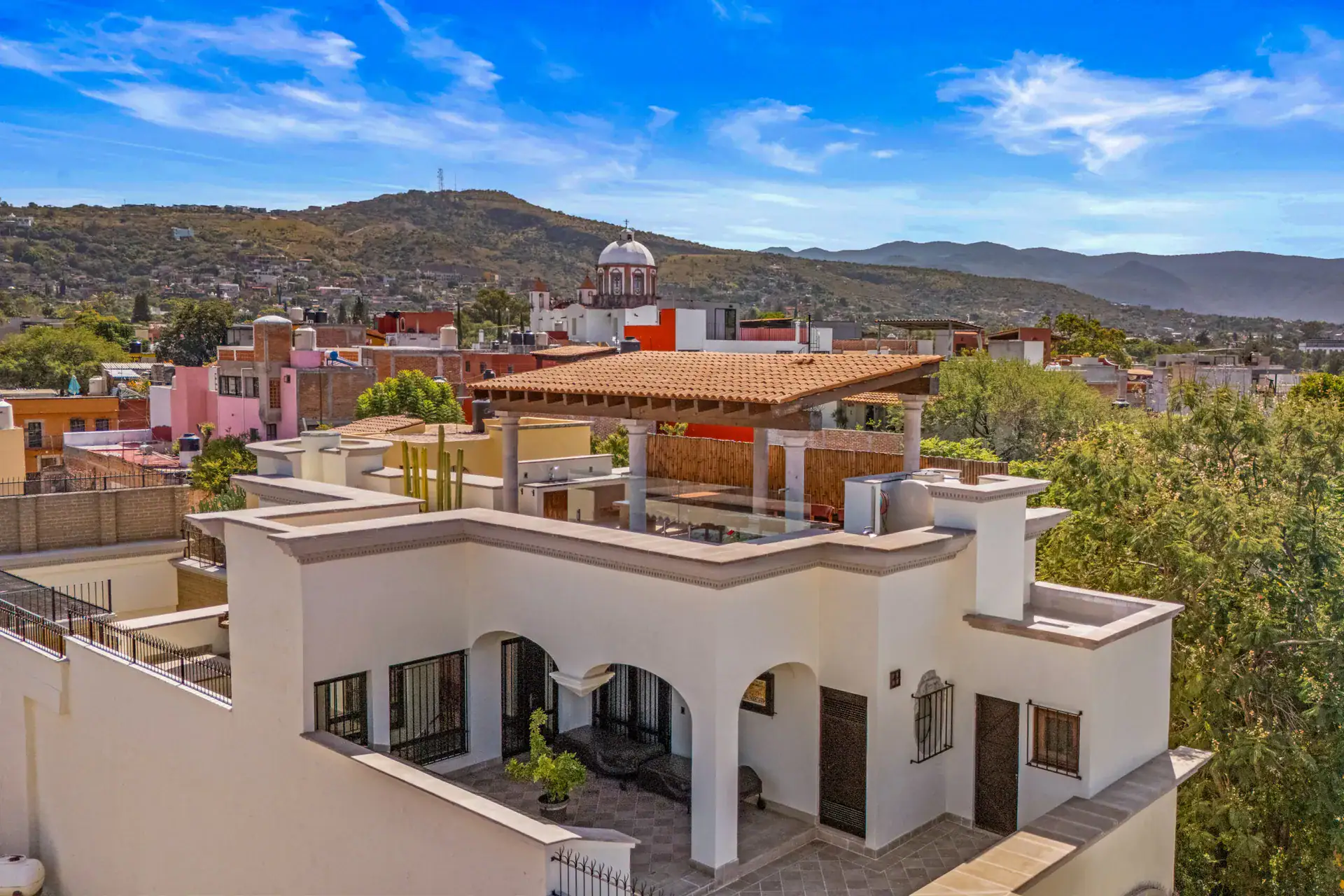 Casa 28 de Abril Norte, rooftop view toward a church dome and the hills with a terracotta-roofed pergola, San Miguel de Allende