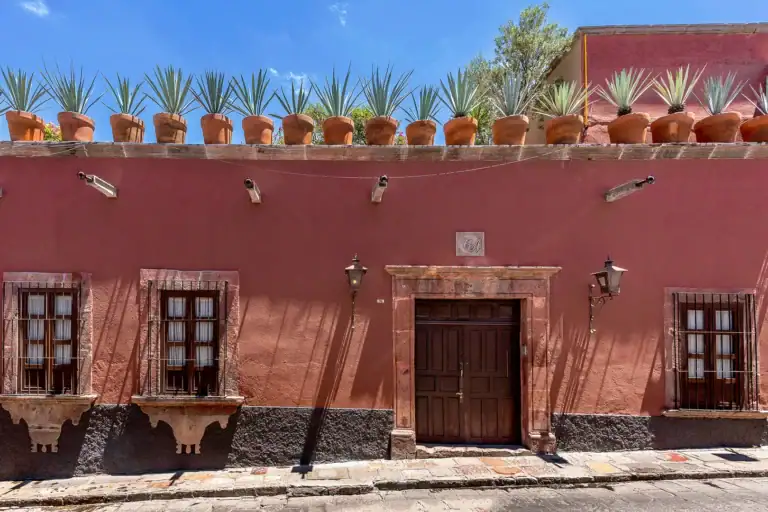 Casa Adelita, red stucco street facade with a wood door and agave plants along the roofline, San Miguel de Allende