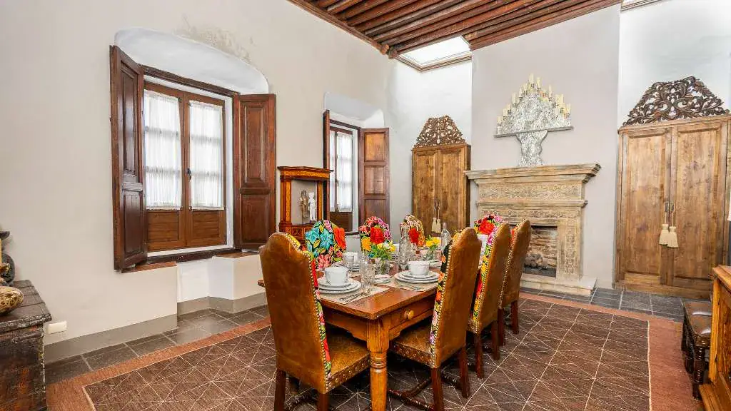 Casa Adelita, dining room with a carved wood table, leather chairs and a stone fireplace, San Miguel de Allende