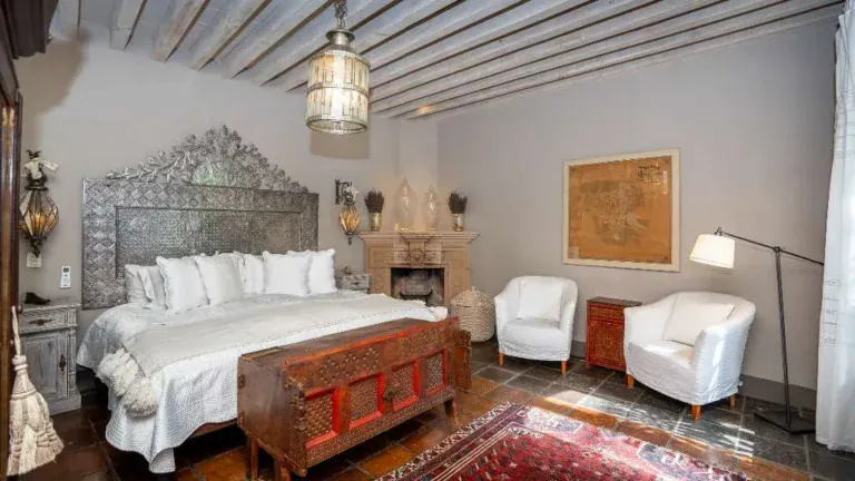 Casa Adelita, primary bedroom with an embossed metal headboard and a stone fireplace, San Miguel de Allende