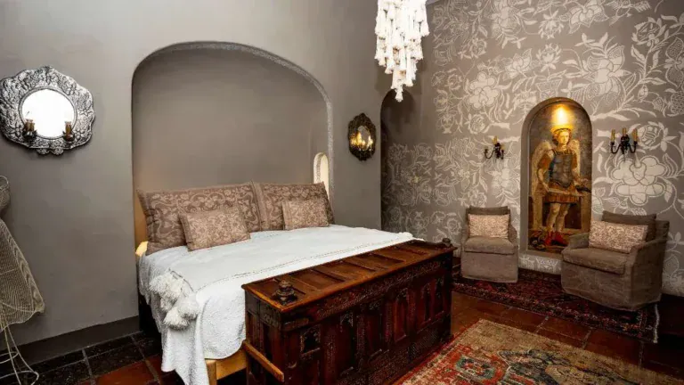 Casa Adelita, bedroom in an arched alcove with a wood trunk and patterned wallpaper, San Miguel de Allende