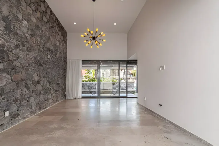 Casa Albero, unfurnished double-height living room with a rough stone wall, a starburst chandelier and a glass wall to the garden, San Miguel de Allende