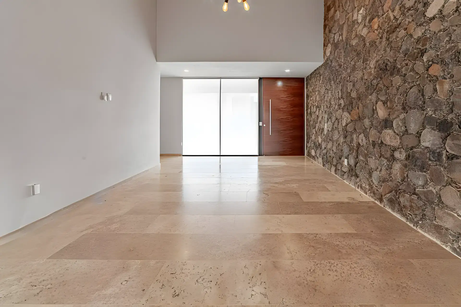 Casa Albero, entry hall with a stone wall, a tall wood front door and a travertine floor, San Miguel de Allende