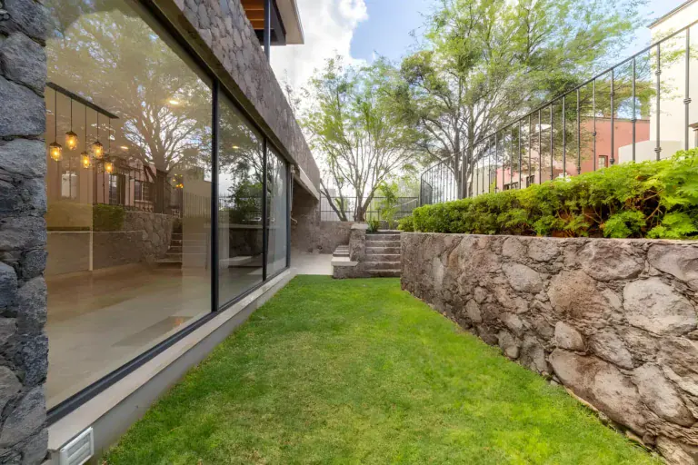 Casa Albero, exterior glass wall of the house along a lawn and a stone retaining wall, San Miguel de Allende