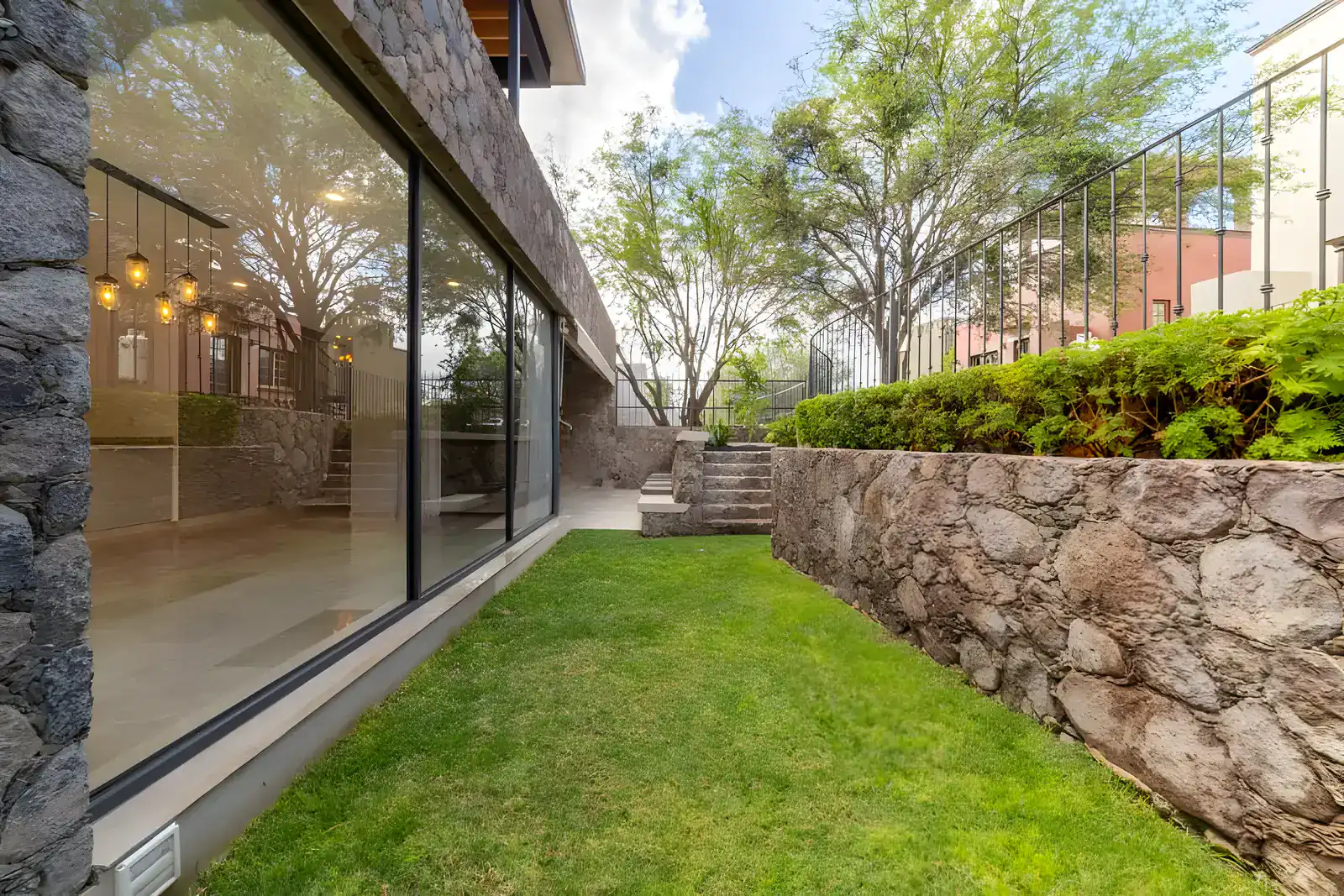 Casa Albero, exterior glass wall of the house along a lawn and a stone retaining wall, San Miguel de Allende