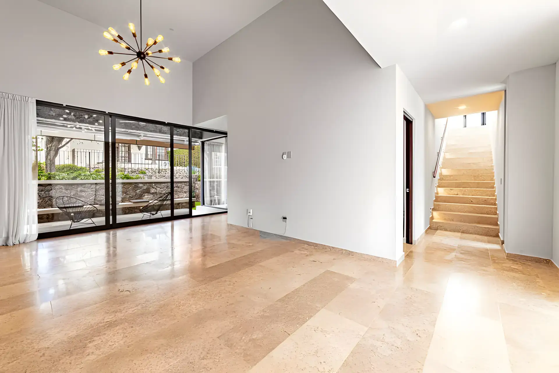 Casa Albero, empty living area with a starburst chandelier, a travertine floor and a staircase going up, San Miguel de Allende