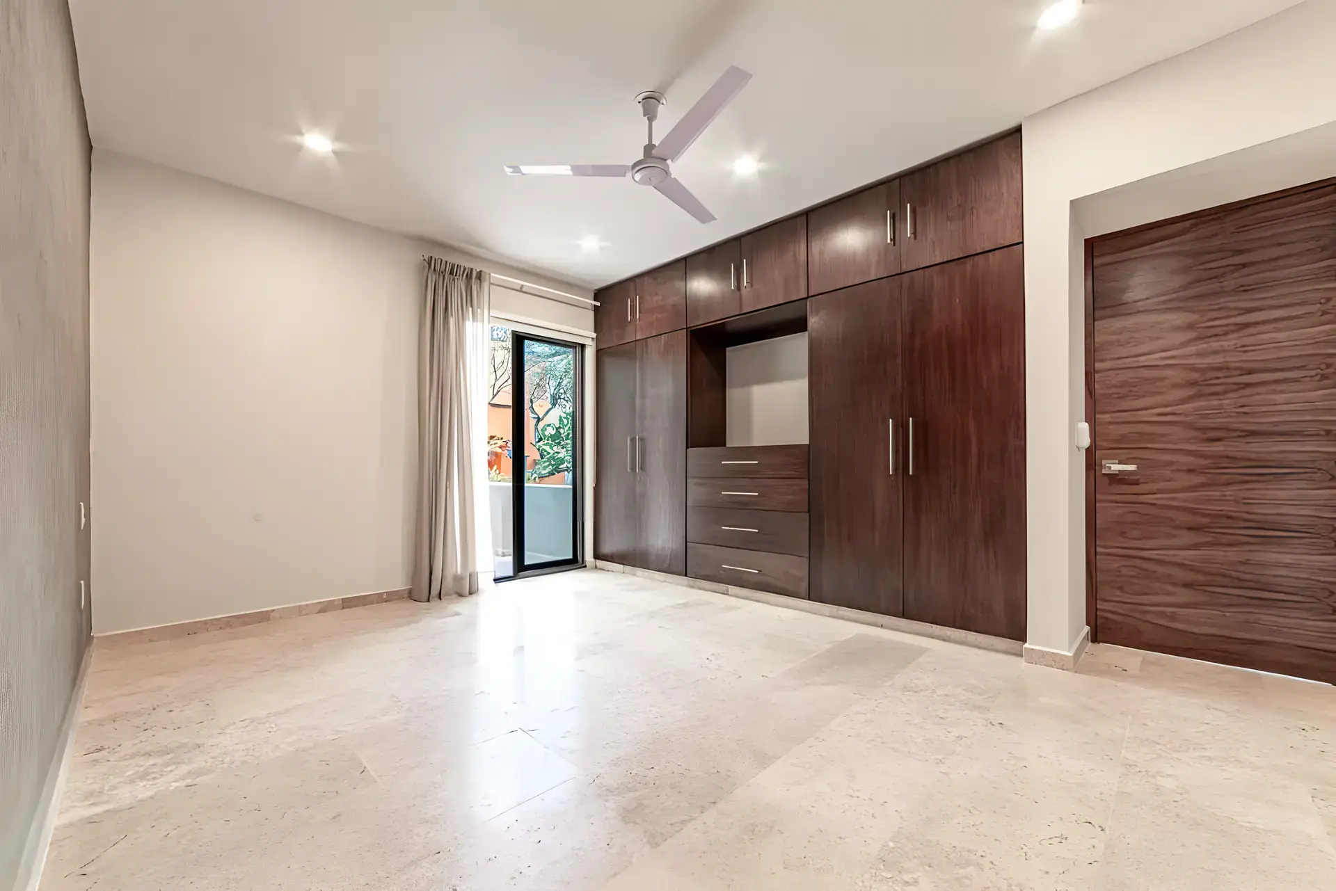 Casa Albero, empty bedroom with a ceiling fan, a wall of wood wardrobes and a glass door to the garden, San Miguel de Allende