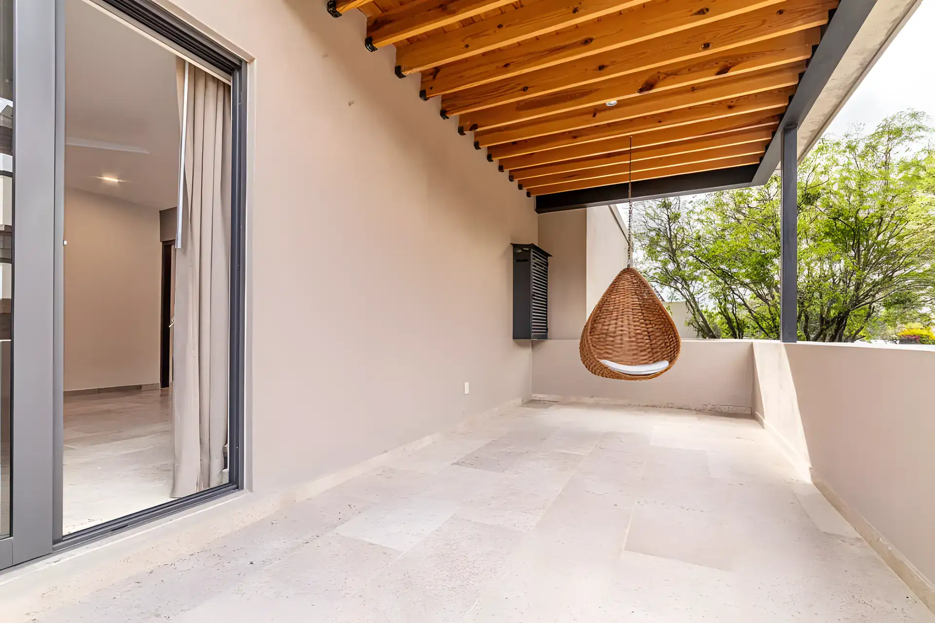 Casa Albero, covered terrace with a wood beam roof, a hanging rattan chair and a sliding glass door, San Miguel de Allende