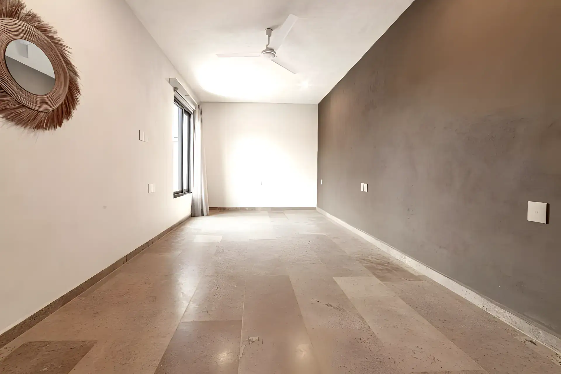 Casa Albero, empty bedroom with a ceiling fan, a brown accent wall and a woven wall mirror, San Miguel de Allende