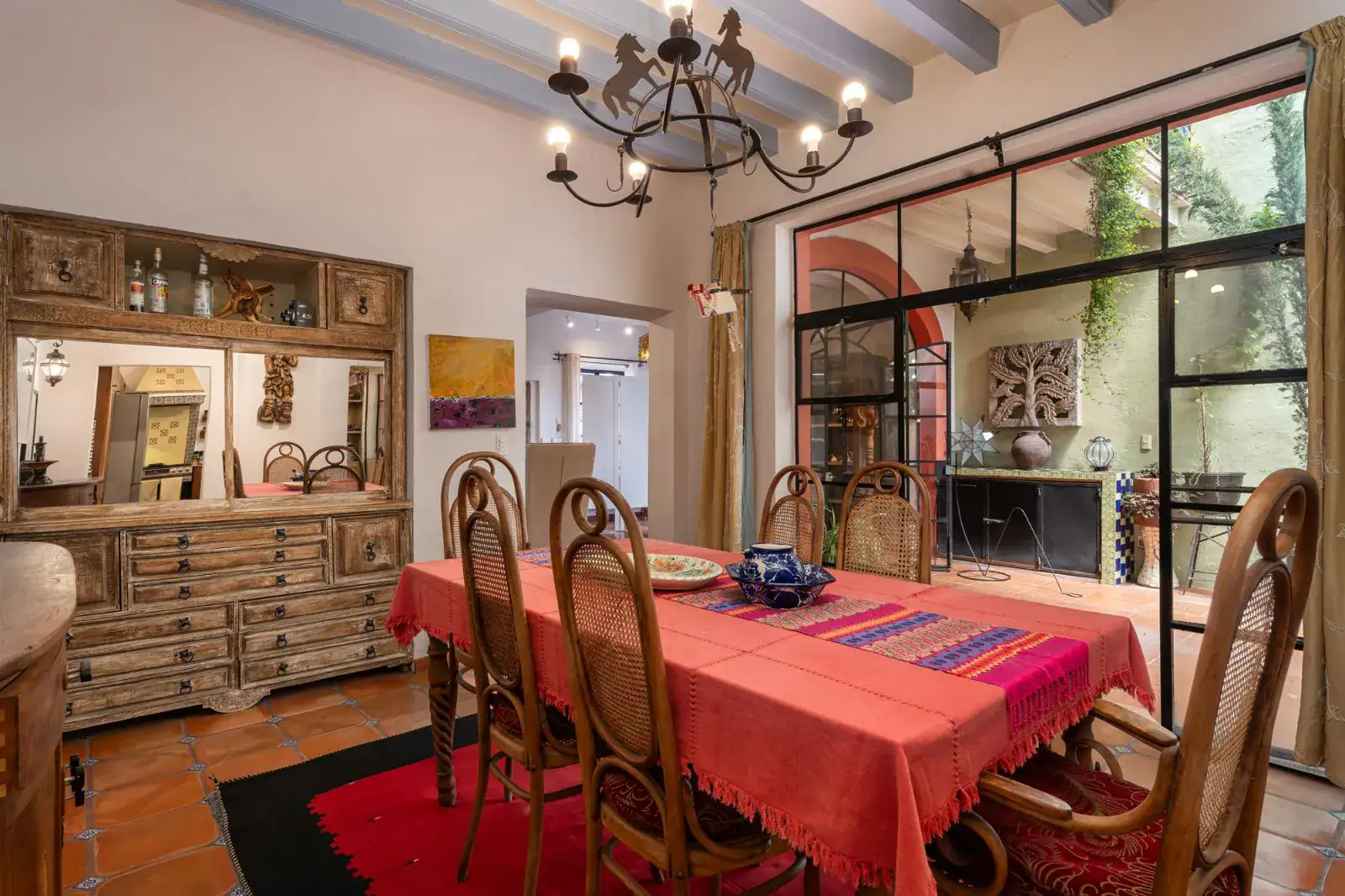 Casa Aldama, dining room with a red tablecloth, wood chairs, a carved sideboard and a steel-framed glass wall, San Miguel de Allende
