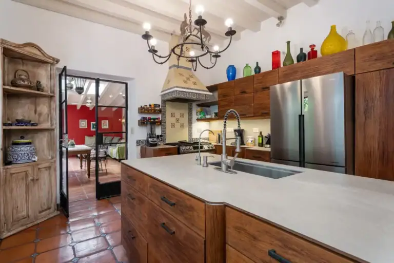 Casa Aldama, kitchen with a wood island, a stainless refrigerator, colorful glass bottles and a view to the dining room, San Miguel de Allende