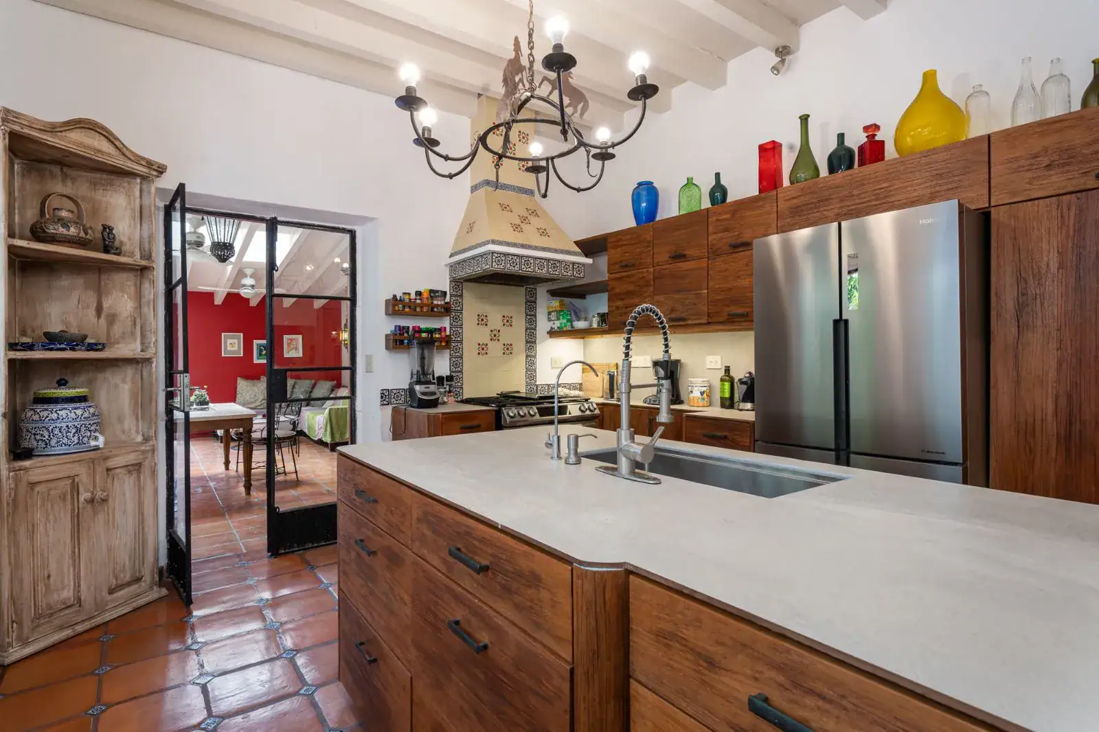 Casa Aldama, kitchen with a wood island, a stainless refrigerator, colorful glass bottles and a view to the dining room, San Miguel de Allende