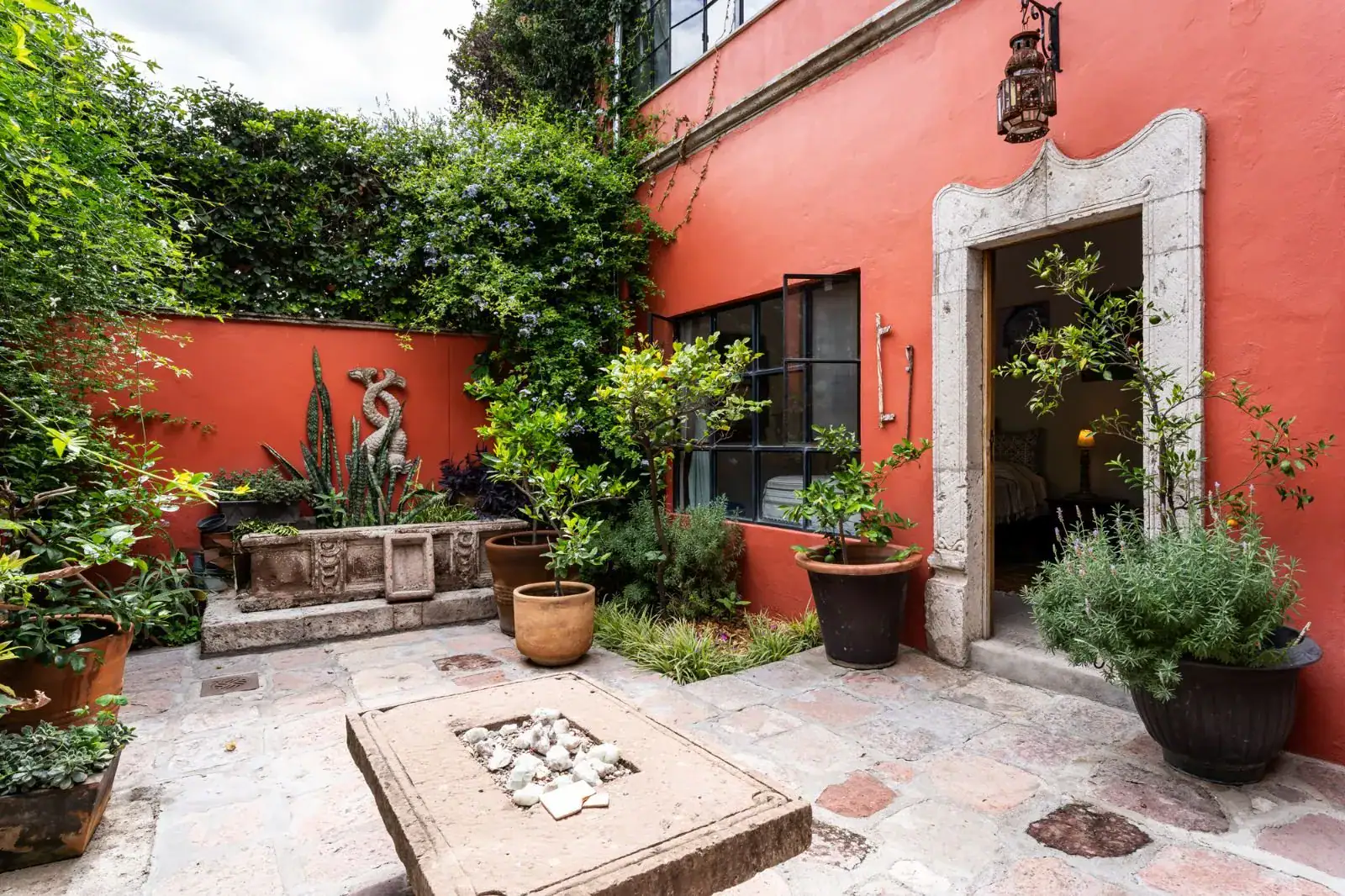 Casa Aldama, courtyard garden with a stone fire table, a red wall and potted plants, San Miguel de Allende
