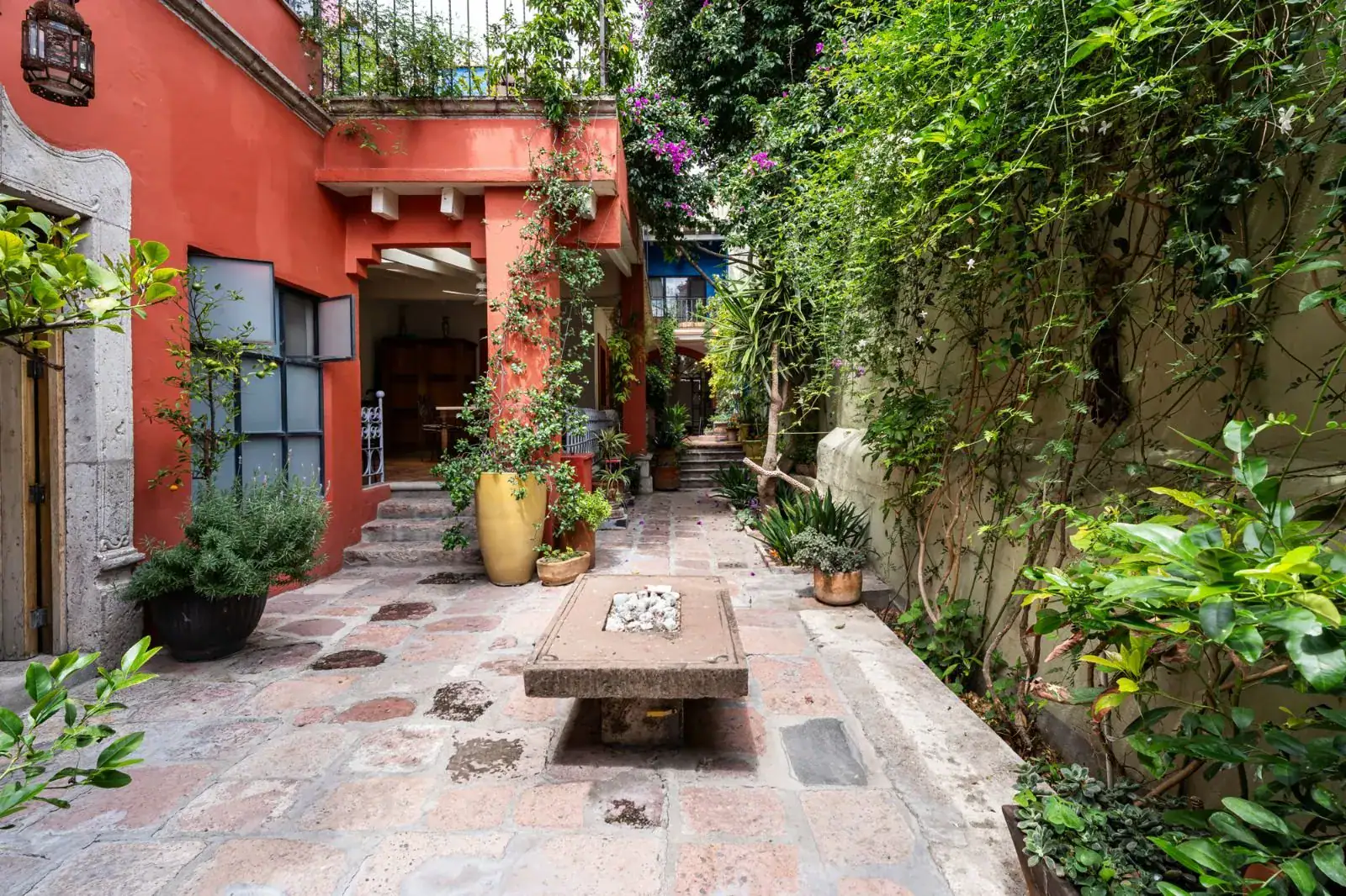Casa Aldama, garden path with a stone table, a red house wall and climbing vines, San Miguel de Allende