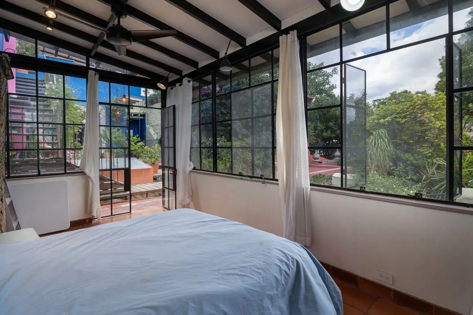 Casa Aldama, bedroom with a steel-framed glass wall and a blue bed, San Miguel de Allende