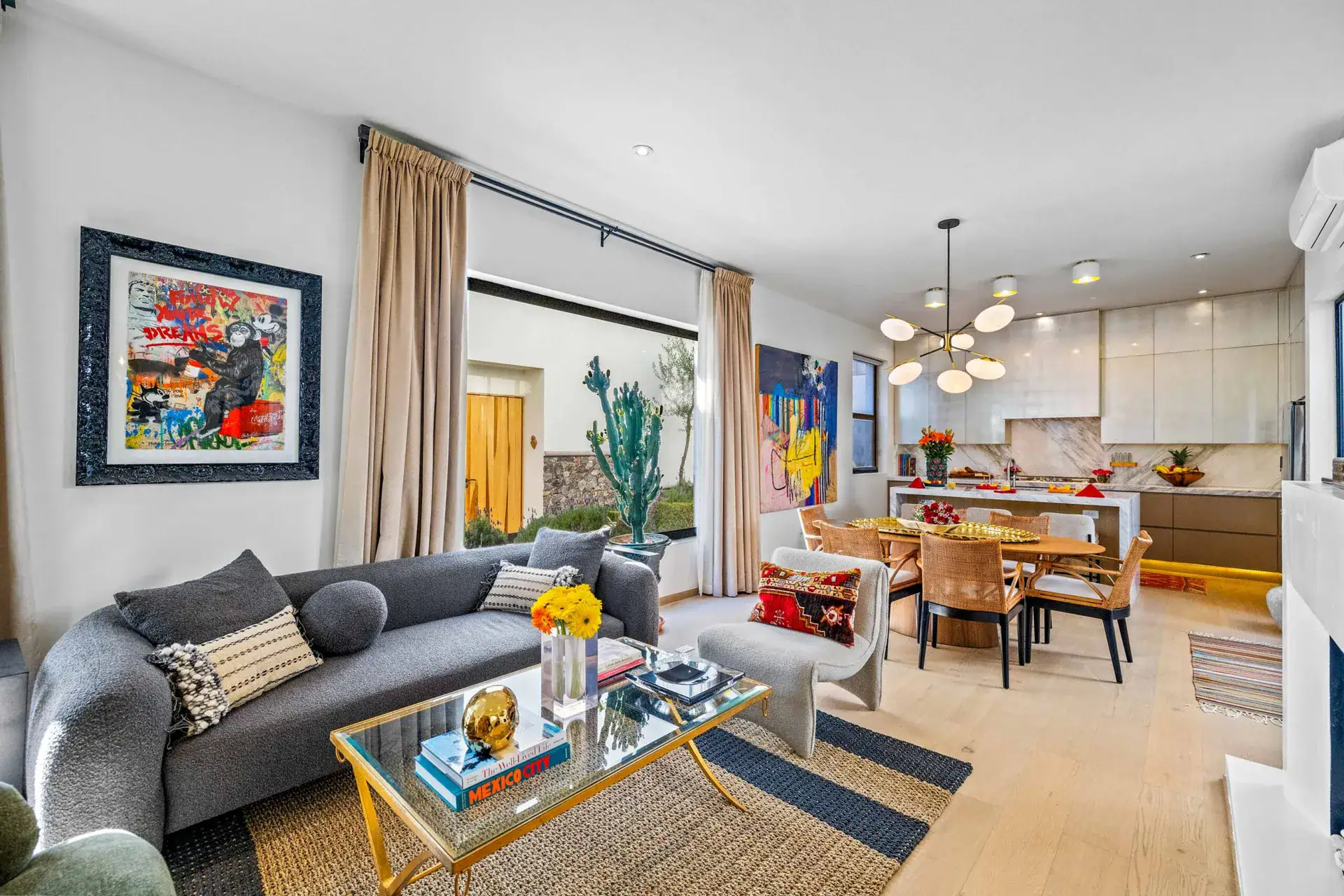 Casa Amoray, living room with a gray sofa, colorful art and an open kitchen behind, San Miguel de Allende