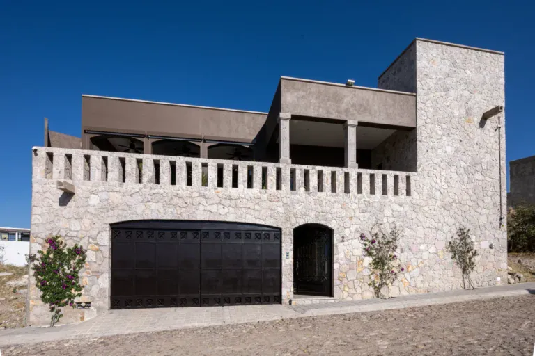 Casa Atardecer, stone and dark stucco house with a balustrade terrace above a dark double garage door and an arched side door, San Miguel de Allende