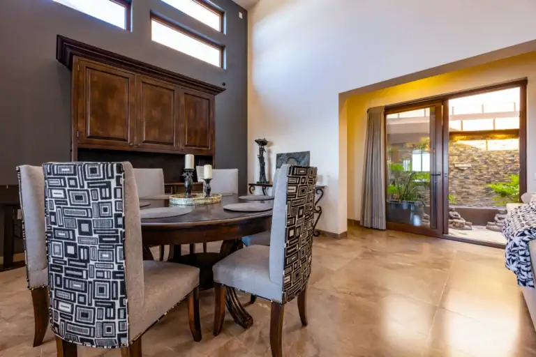 Casa Atardecer, dining table with patterned upholstered chairs below clerestory windows and a carved wood cabinet, with a patio door beyond, San Miguel de Allende
