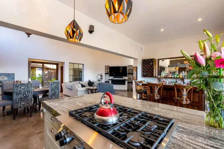 Casa Atardecer, kitchen island with a gas cooktop and a red kettle, looking across to the dining and living areas and a home bar, San Miguel de Allende
