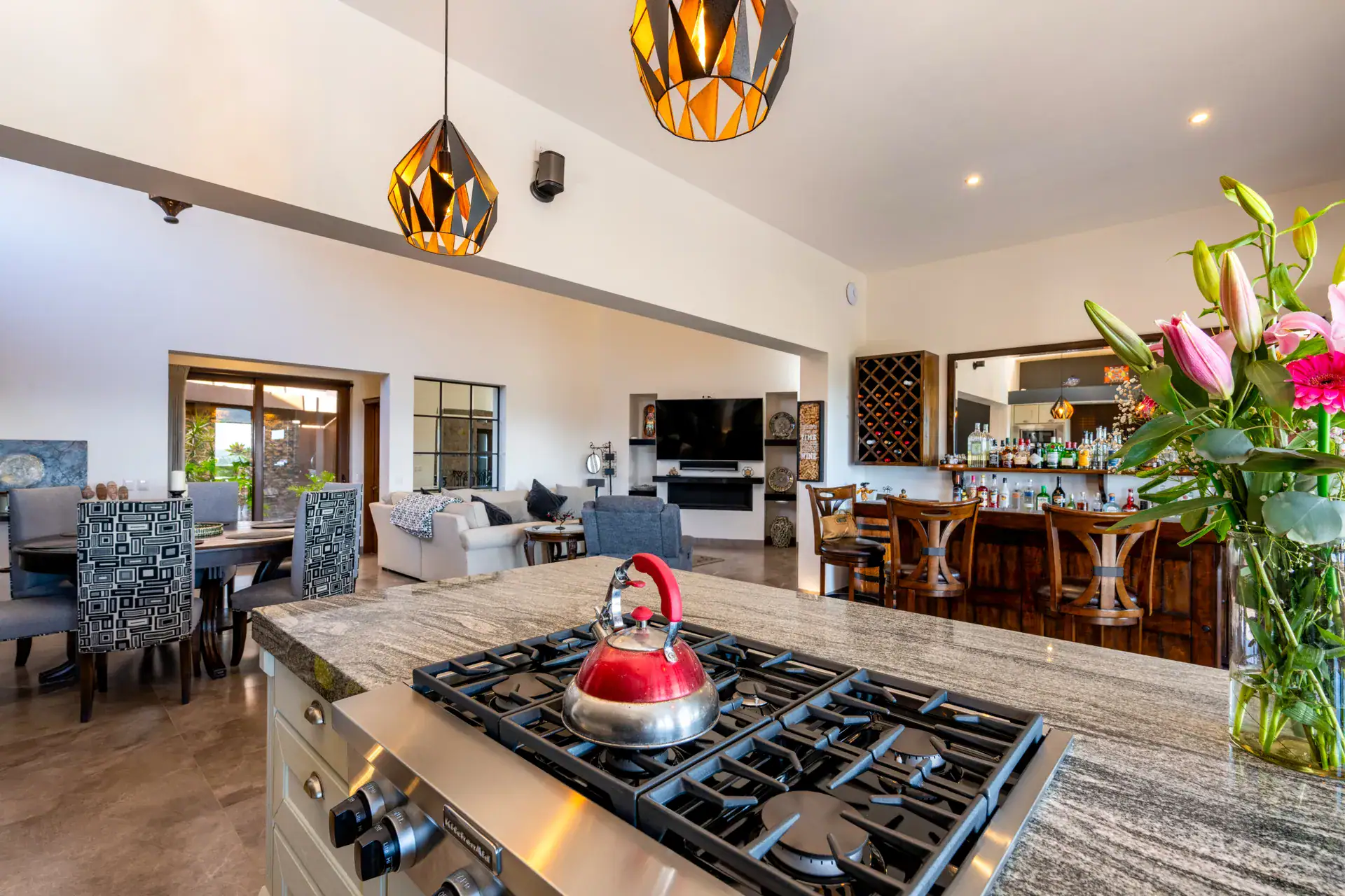 Casa Atardecer, kitchen island with a gas cooktop and a red kettle, looking across to the dining and living areas and a home bar, San Miguel de Allende