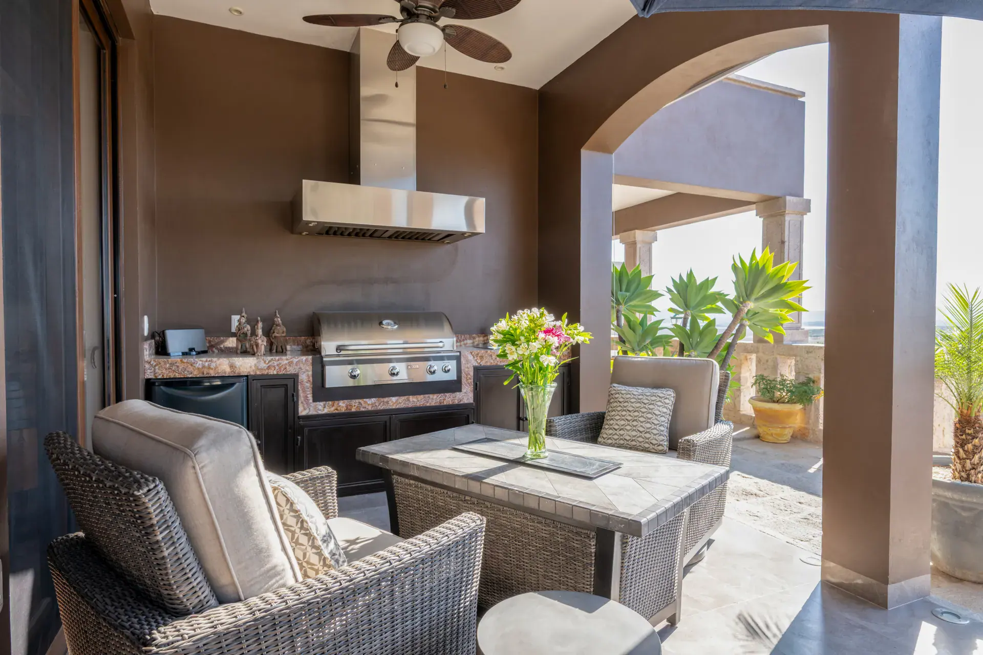 Casa Atardecer, covered terrace with an outdoor kitchen with a built-in grill and wicker lounge chairs around a stone fire table, San Miguel de Allende