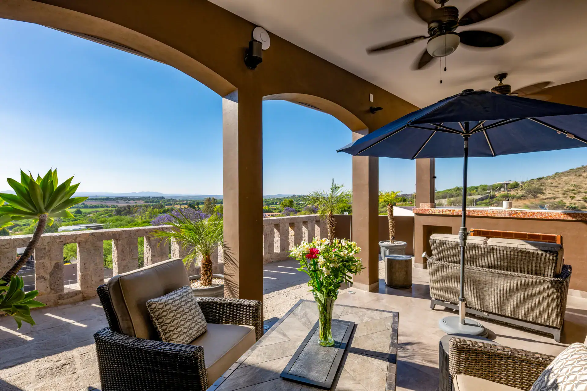 Casa Atardecer, terrace under arches with wicker sofas, a navy umbrella and a view of fields and distant mountains, San Miguel de Allende