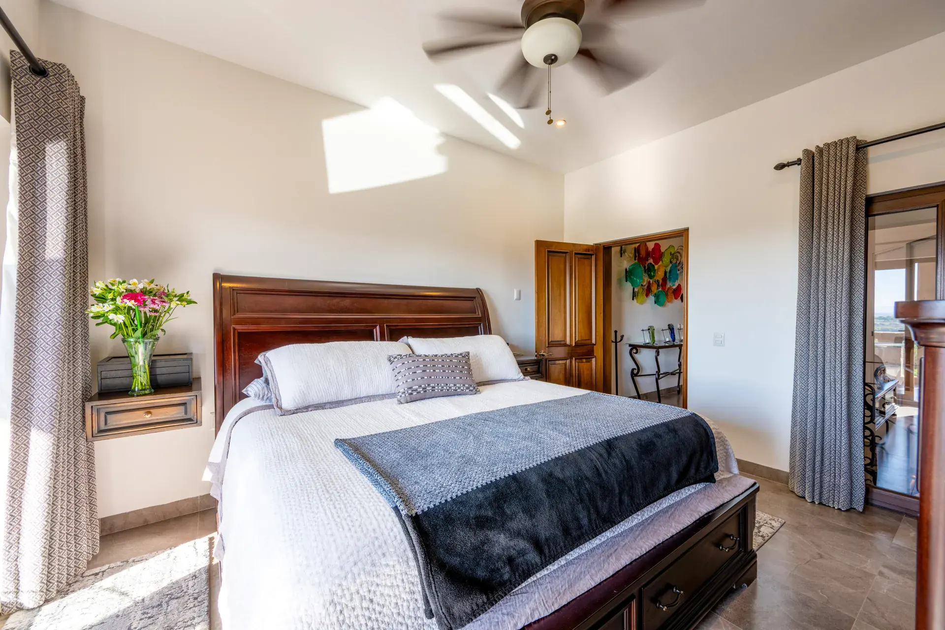 Casa Atardecer, bedroom with a wood sleigh bed, a gray throw, a ceiling fan and balcony doors with curtains, San Miguel de Allende