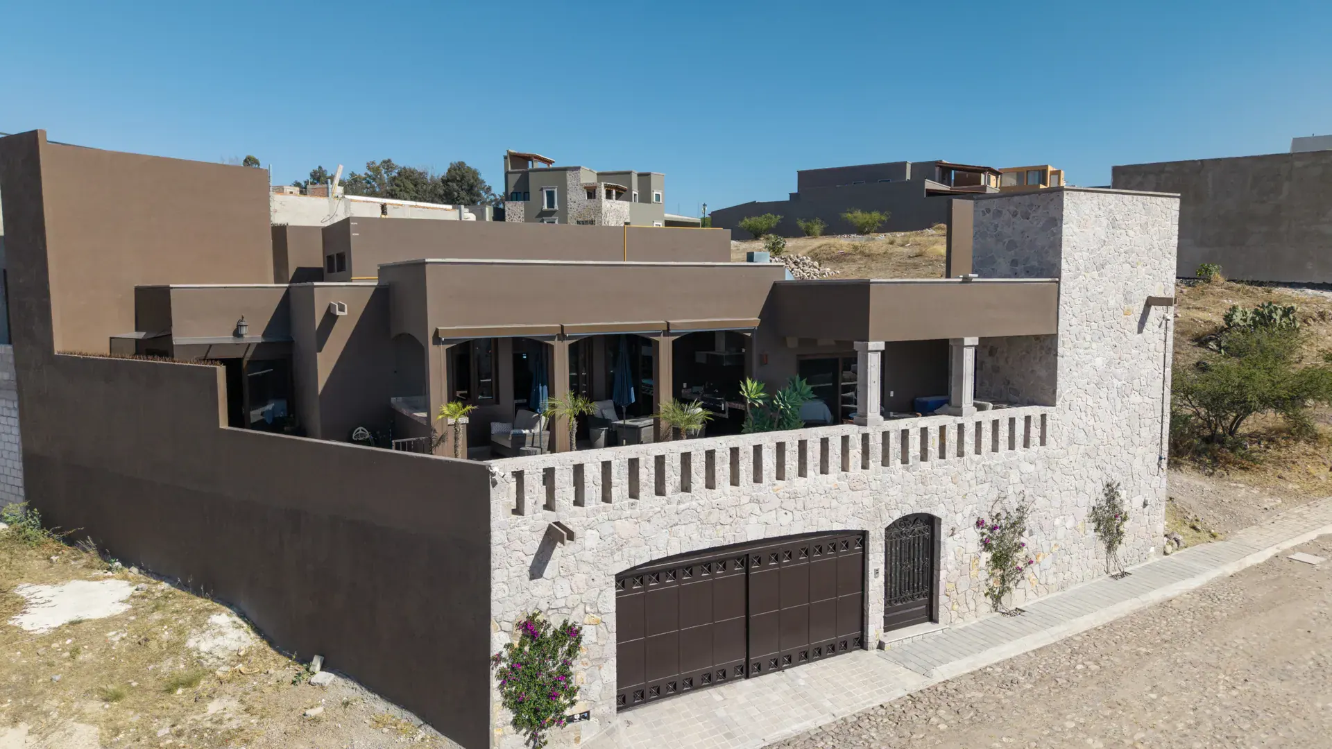 Casa Atardecer, aerial view of the house with a stone terrace wall, a dark garage and the covered terrace on the hillside, San Miguel de Allende