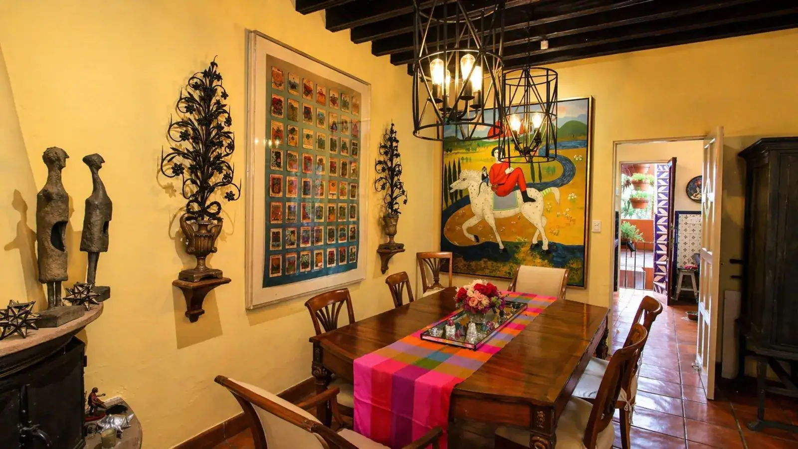 Casa Baeza, dining room with a wood table, pink striped runner, iron chandeliers and a colorful horse painting, San Miguel de Allende