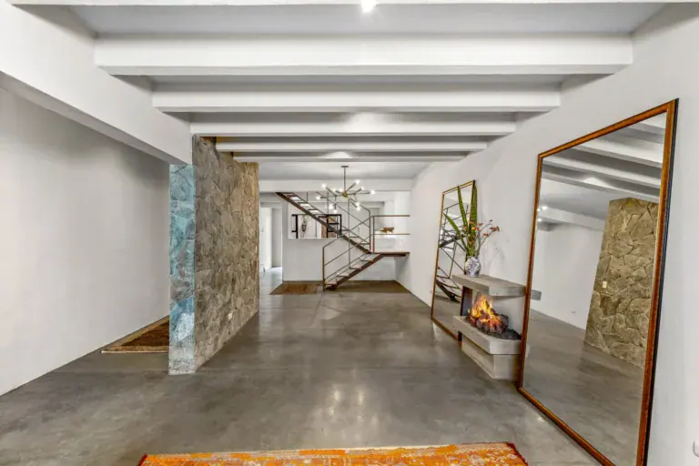 Casa Beatrice, long open ground floor with white beams, a stone feature wall, a floating stair and a wall fireplace with tall mirrors, San Miguel de Allende