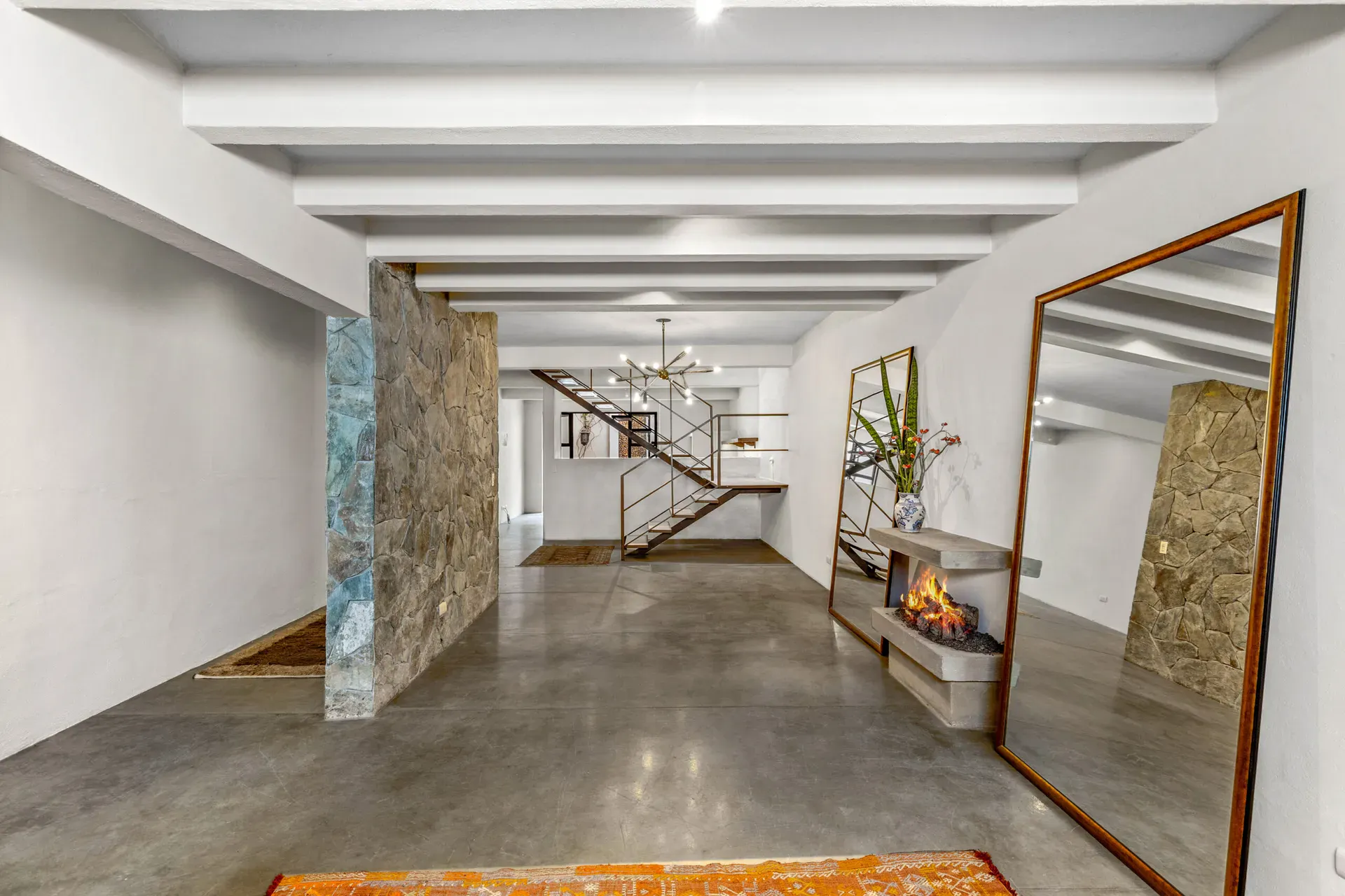 Casa Beatrice, long open ground floor with white beams, a stone feature wall, a floating stair and a wall fireplace with tall mirrors, San Miguel de Allende