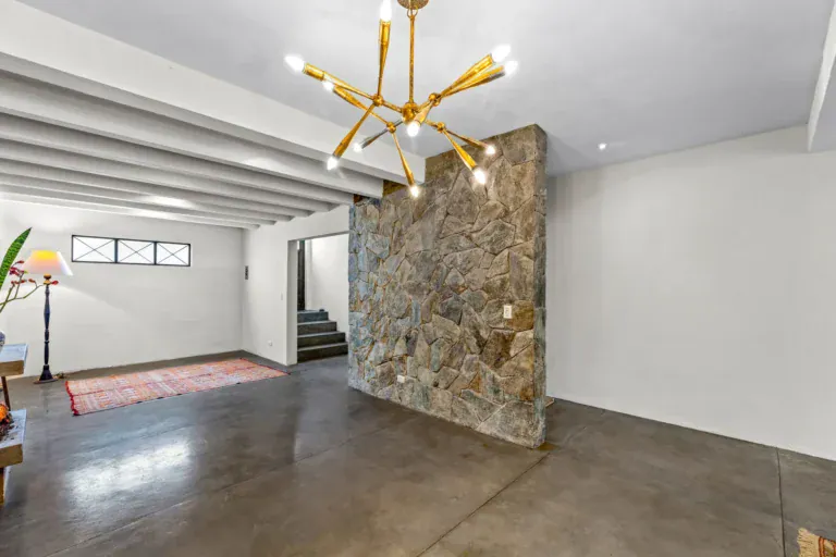 Casa Beatrice, empty living area with a gold sputnik chandelier, a stone feature wall, white beams and a stair, San Miguel de Allende