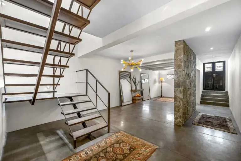 Casa Beatrice, floating stair with a dark wood and steel frame, a gold chandelier and an entry door with a stone wall, San Miguel de Allende