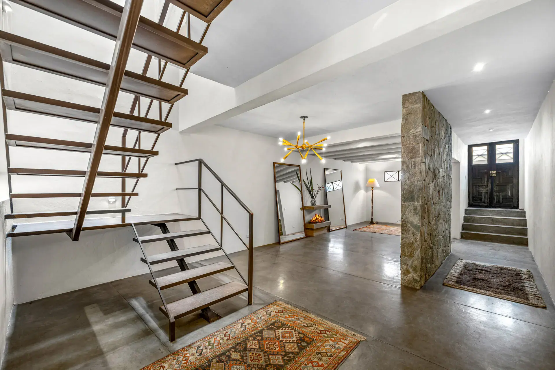 Casa Beatrice, floating stair with a dark wood and steel frame, a gold chandelier and an entry door with a stone wall, San Miguel de Allende