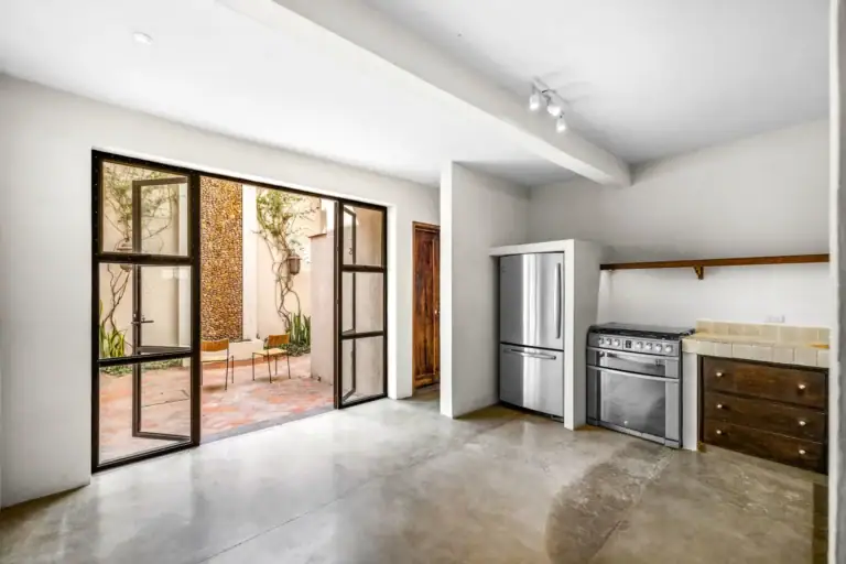 Casa Beatrice, empty kitchen with a stainless refrigerator, a gas range, dark wood cabinets and a steel-framed glass wall to the patio, San Miguel de Allende