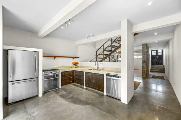 Casa Beatrice, kitchen with a stainless refrigerator, a range, a dishwasher, wood cabinets and the entry hall beyond, San Miguel de Allende