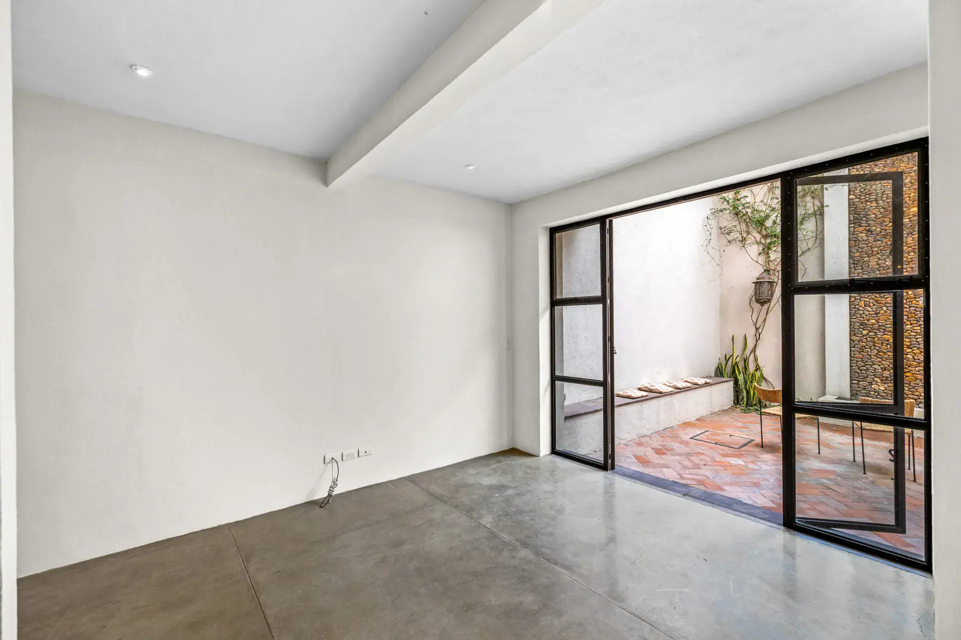 Casa Beatrice, empty room with a polished concrete floor and a steel-framed sliding glass door to the courtyard, San Miguel de Allende
