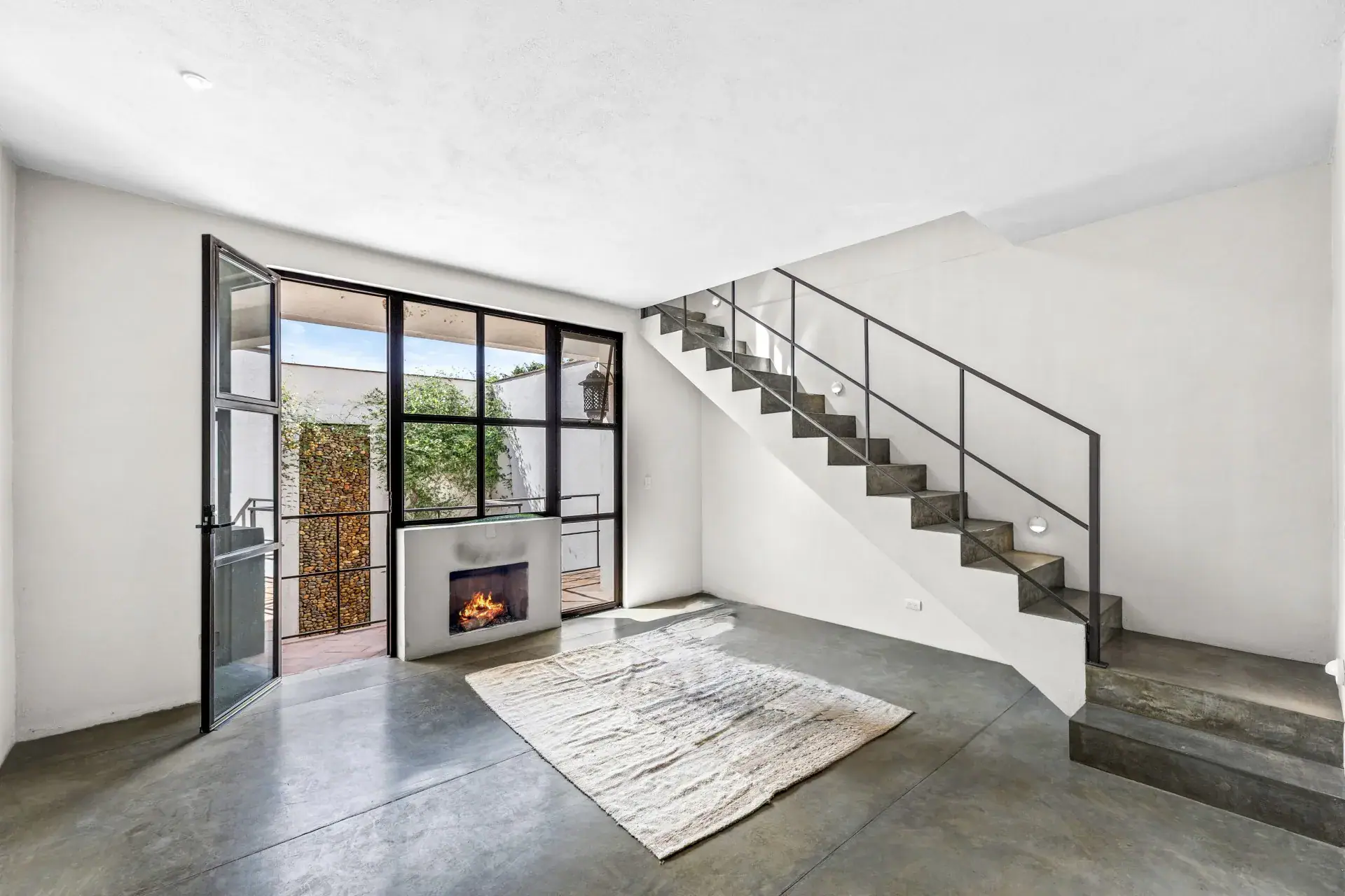 Casa Beatrice, empty studio room with a steel stair, a fireplace, steel-framed glass doors and a concrete floor, San Miguel de Allende