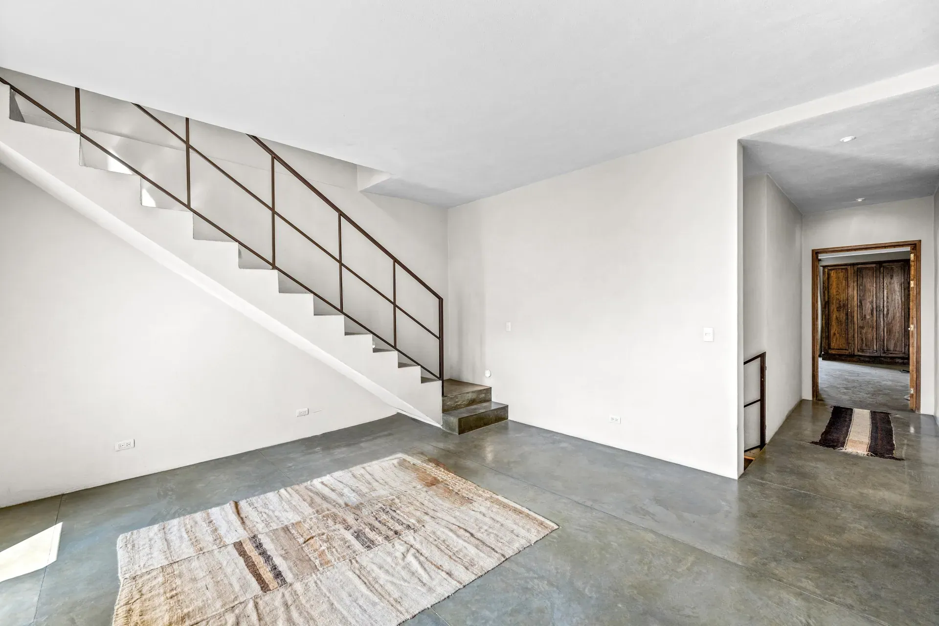 Casa Beatrice, empty room with a steel and concrete stair, a rug and a carved wood door, San Miguel de Allende