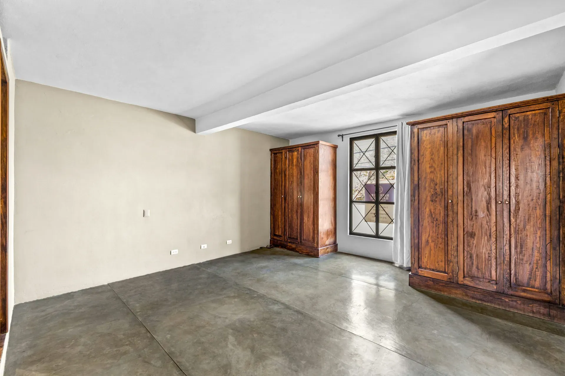 Casa Beatrice, empty bedroom with two carved wood armoires, a window with a leaded grille and a concrete floor, San Miguel de Allende