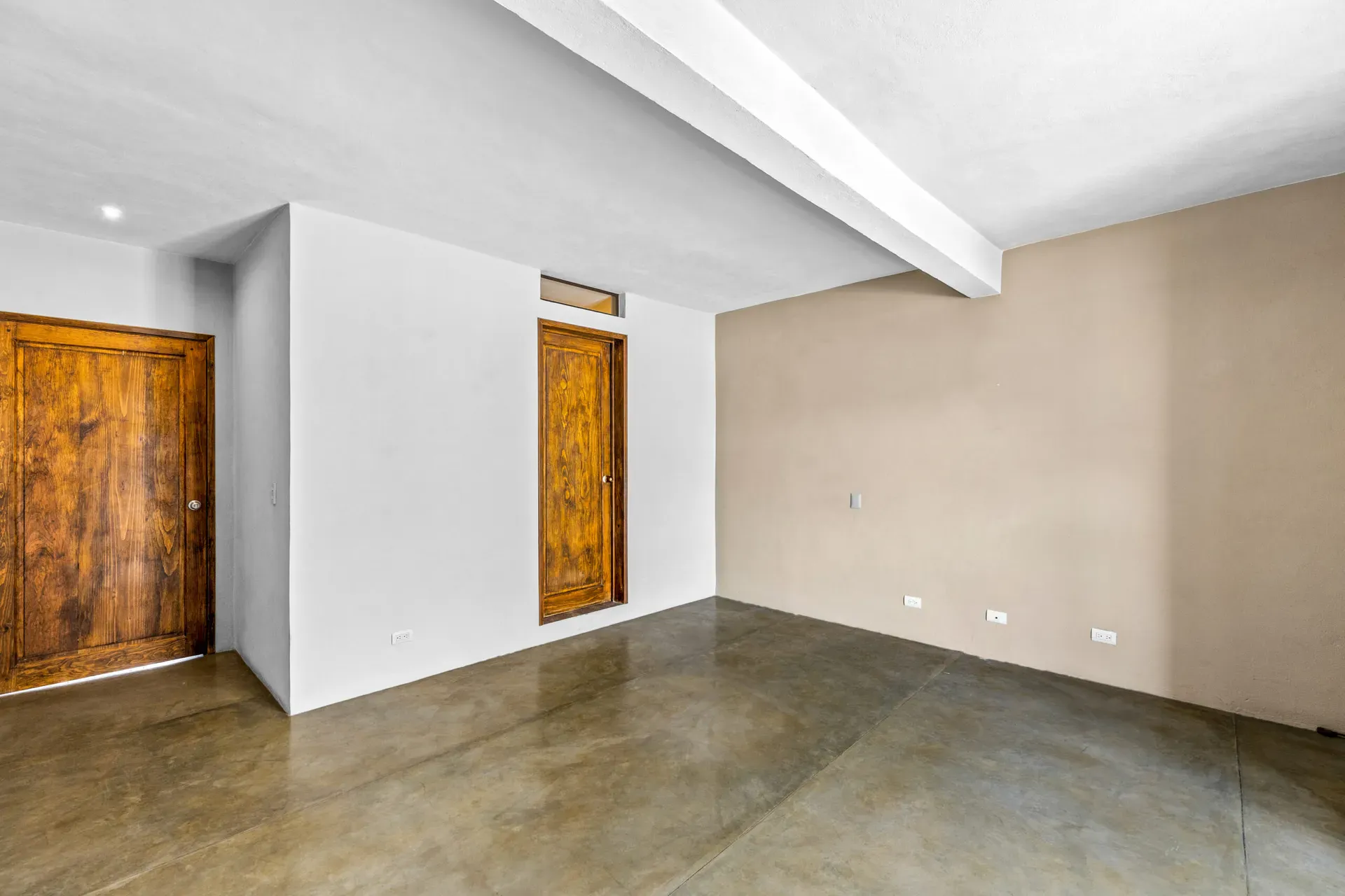 Casa Beatrice, empty bedroom with a carved wood door, a beam and a concrete floor, San Miguel de Allende