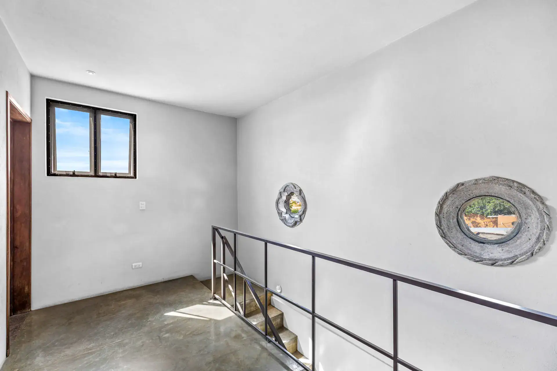 Casa Beatrice, empty room at the stair top with a steel railing, two round stone mirrors and a window, San Miguel de Allende