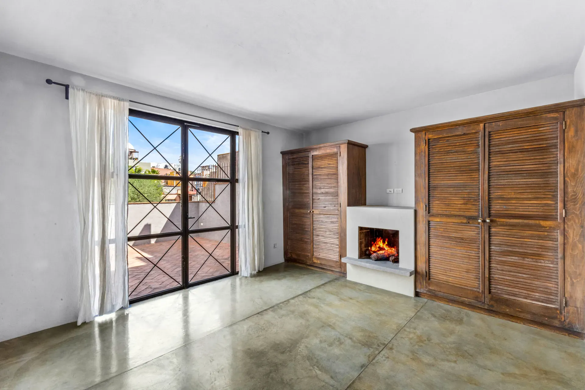 Casa Beatrice, empty bedroom with a fireplace, a wood louvered wardrobe and steel-framed glass doors with a view of the roof terrace, San Miguel de Allende