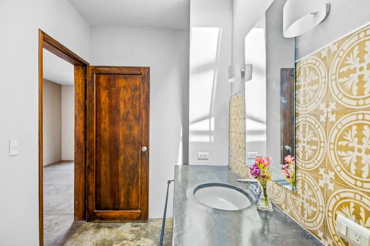 Casa Beatrice, bathroom doorway with a carved wood door, a patterned tile wall and a metal sink, San Miguel de Allende